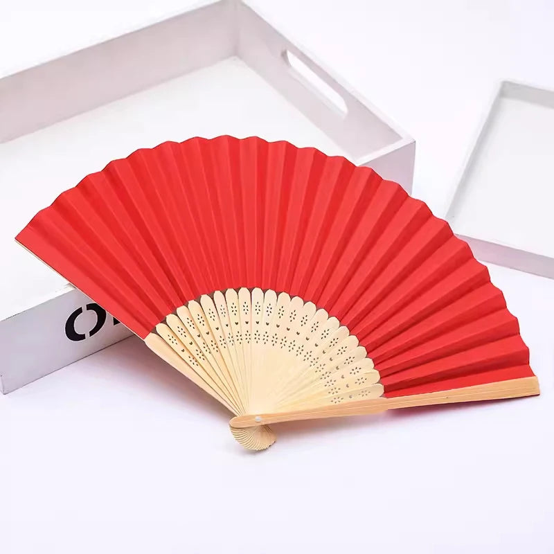 Un éventail pliable à la main avec des nervures en bambou et du papier rouge, sur fond blanc.