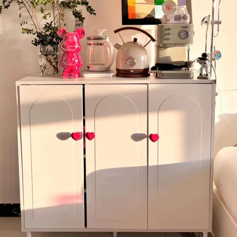 A white cabinet with arched doors displays a heart-shaped toilet presser button and various kitchen gadgets.