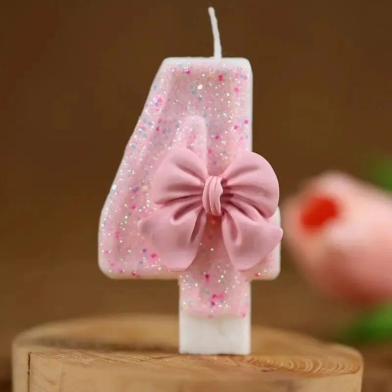 A pink glitter number candle shaped like the number 4 with a bow on a wooden surface.