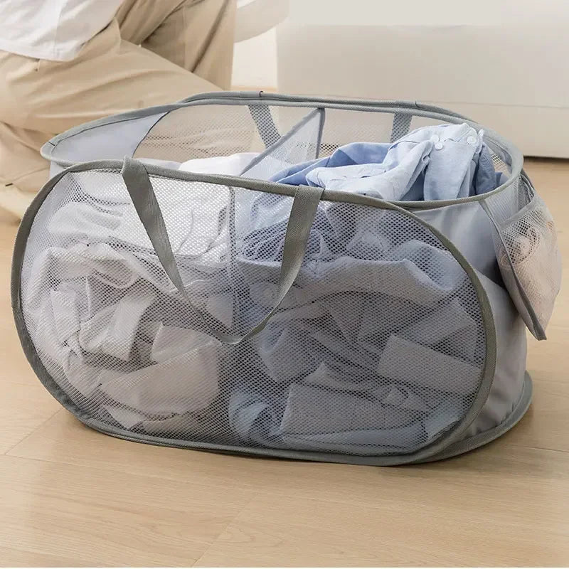A gray foldable mesh laundry basket filled with folded blue and white clothes on a wooden floor.