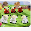 A collection of resin highland cow figurines in various colors and sizes displayed on green grass.