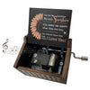 A small wooden music box with a lid featuring text about sunshine and love, set in a dark wooden box.