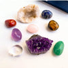A collection of natural crystals including amethyst, citrine, blue sapphire, rose quartz, and green jade stones.