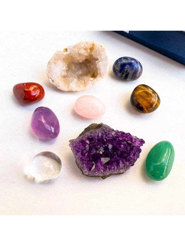A collection of natural crystals including amethyst, citrine, blue sapphire, rose quartz, and green jade stones.