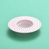 A pink kitchen sink drain strainer with a perforated mesh design is shown against a light green background.