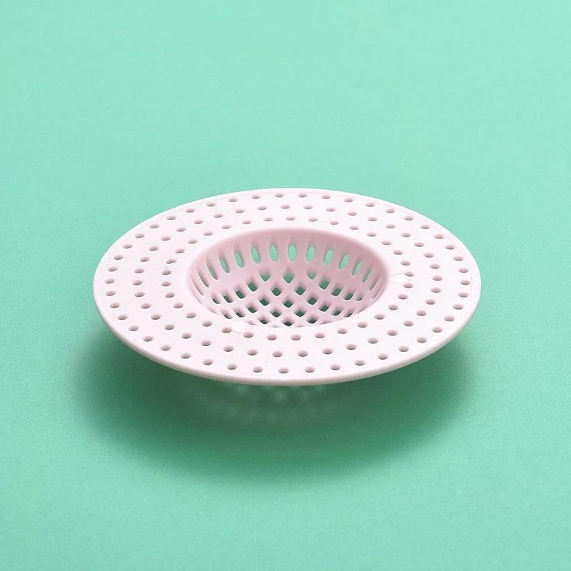 A pink kitchen sink drain strainer with a perforated mesh design is shown against a light green background.