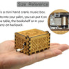 A small, rectangular wooden music box with intricate engraving is held in a person's palm.