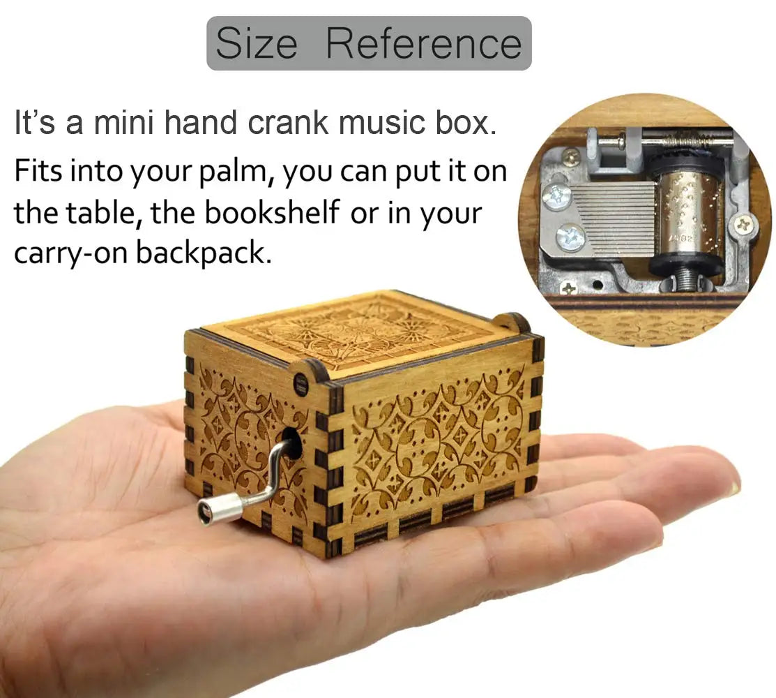 A small, rectangular wooden music box with intricate engraving is held in a person's palm.