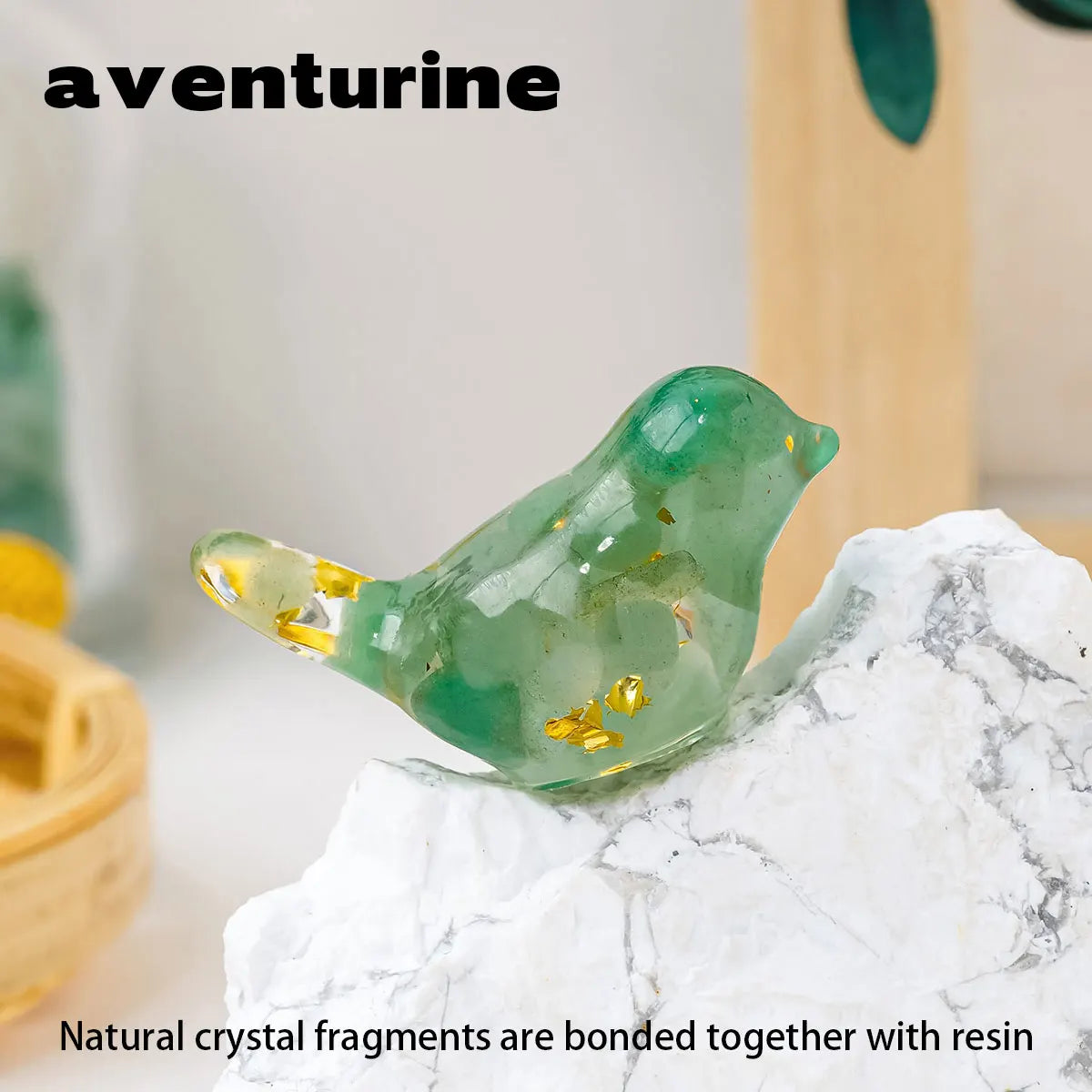 A small, translucent green crystal bird statue with gold inclusions resting on a white rock.