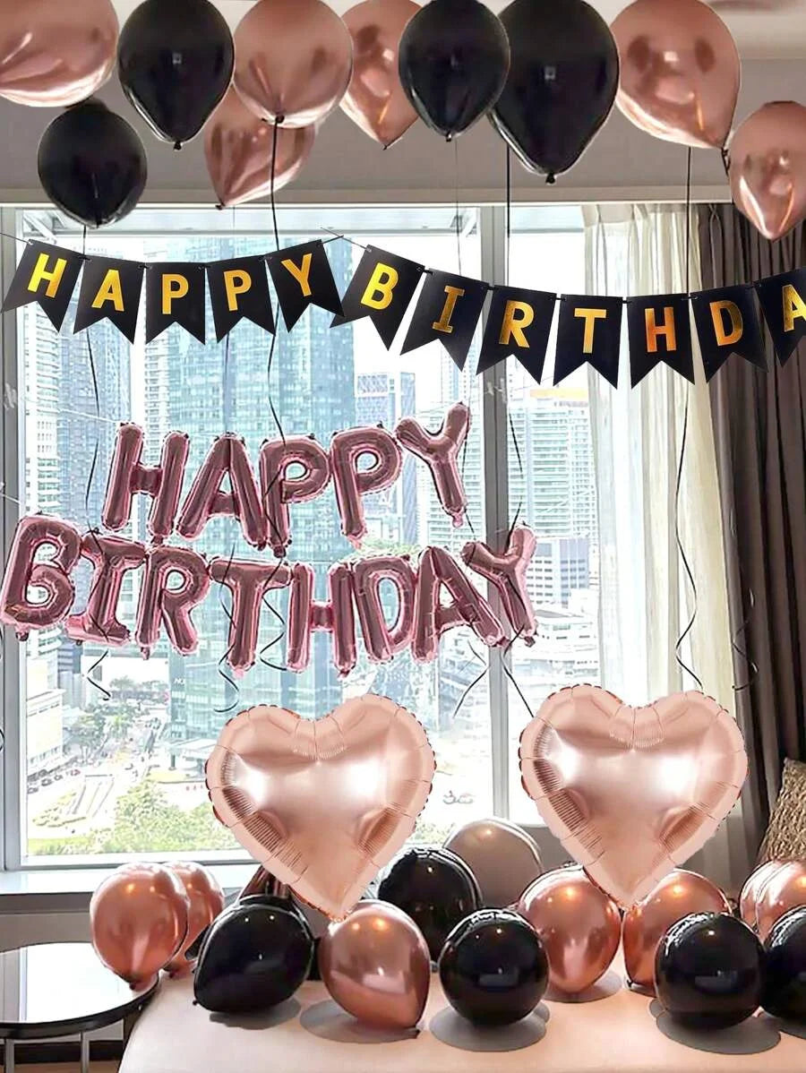 A celebration setup featuring foil balloons spelling out Happy Birthday and heart-shaped balloons in rose gold and black.