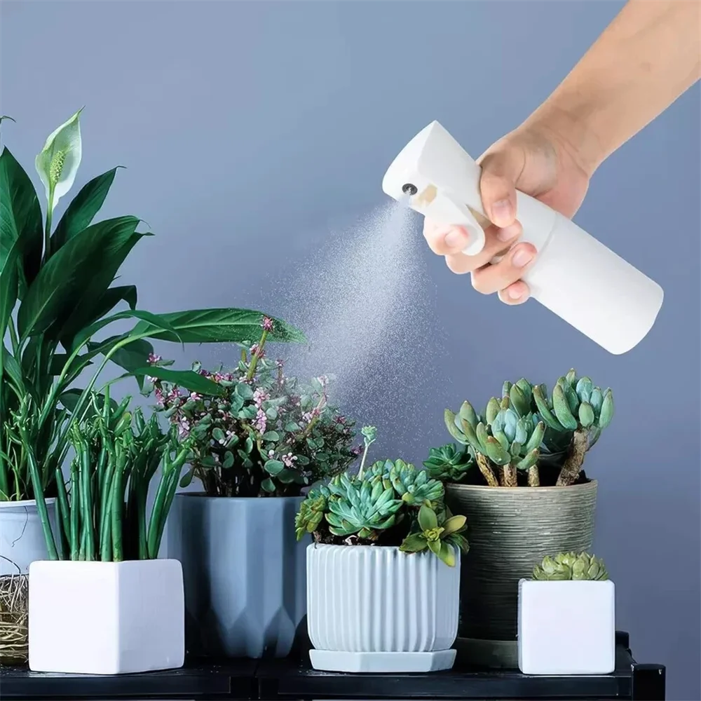 A hand sprays a fine mist from a white handheld spray bottle over potted green plants.