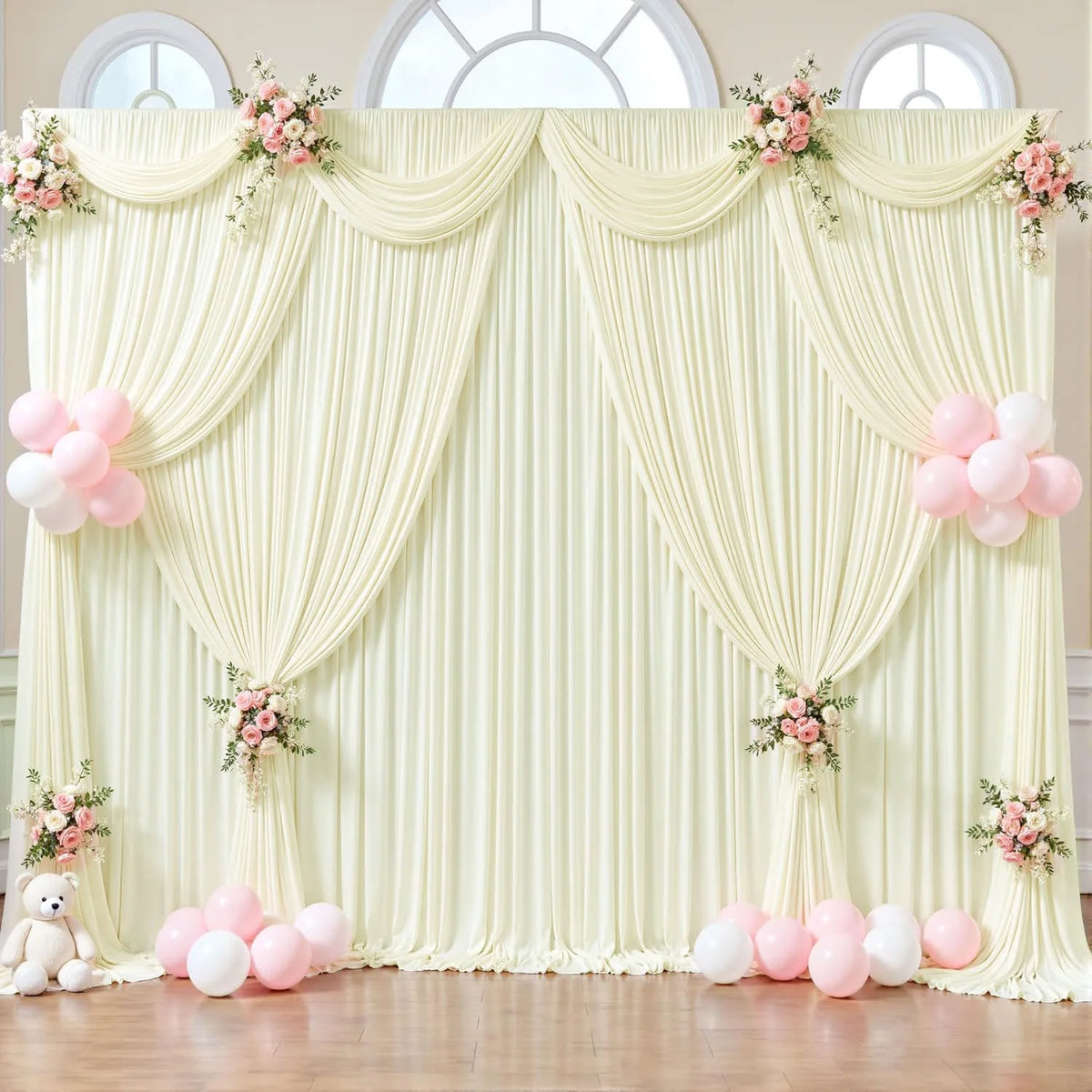Fondo de tela crema decorado con cortinas drapeadas y toques florales rosas para un evento.