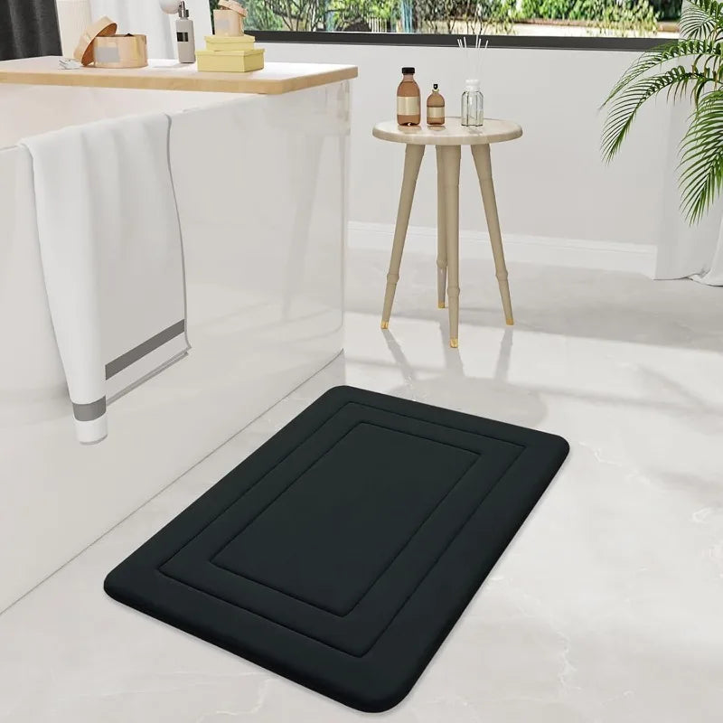 A black non-slip absorbent bath mat is placed on a light floor next to a white counter and a small wooden table.