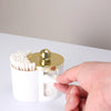 A hand is holding a white plastic bathroom organizer with a gold lid, showing cotton swabs inside.