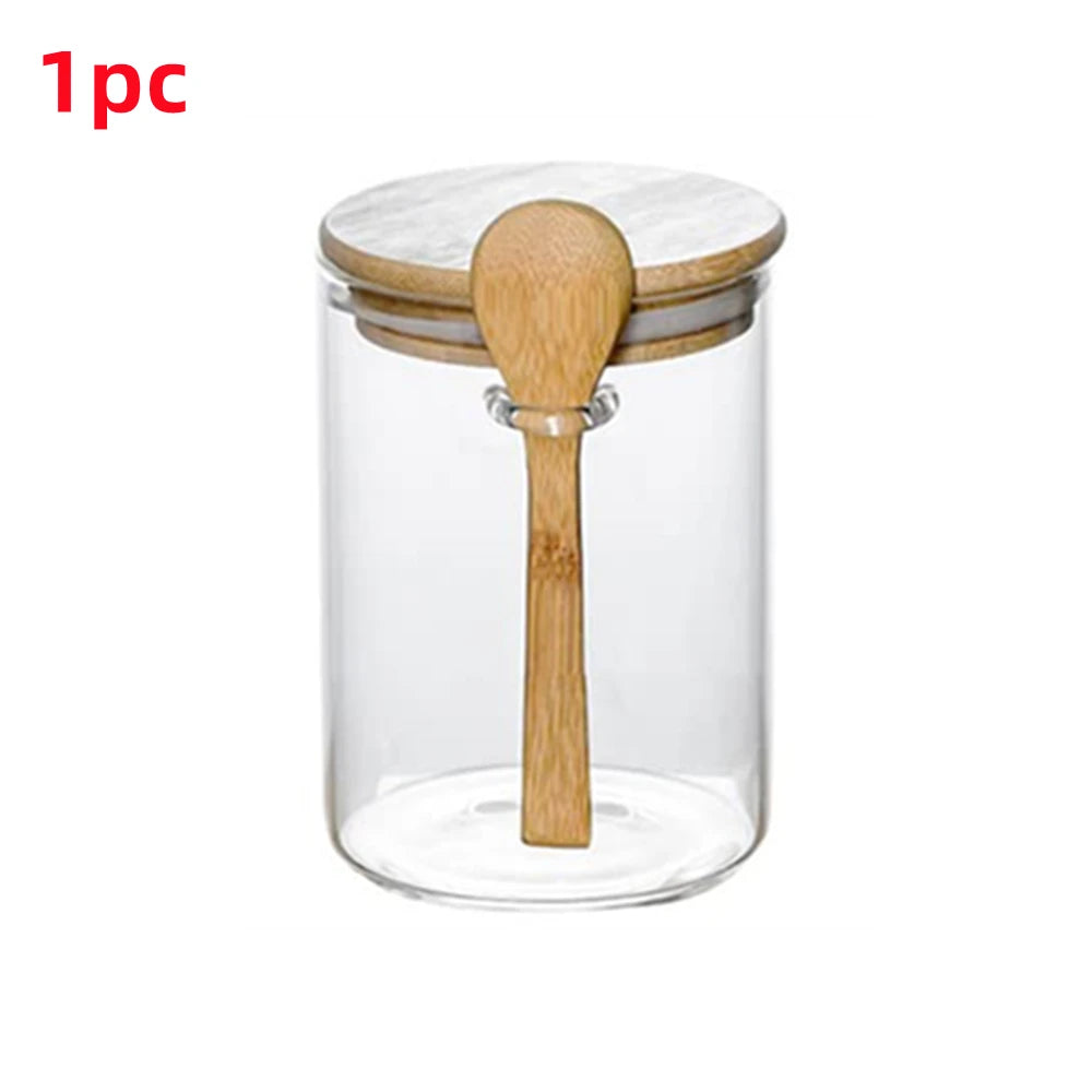 A clear glass spice jar with a bamboo lid and wooden spoon inside.