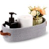 A woven cotton storage basket holds a black soap dispenser, a roll of white paper towels, and a bouquet of orange and cream f