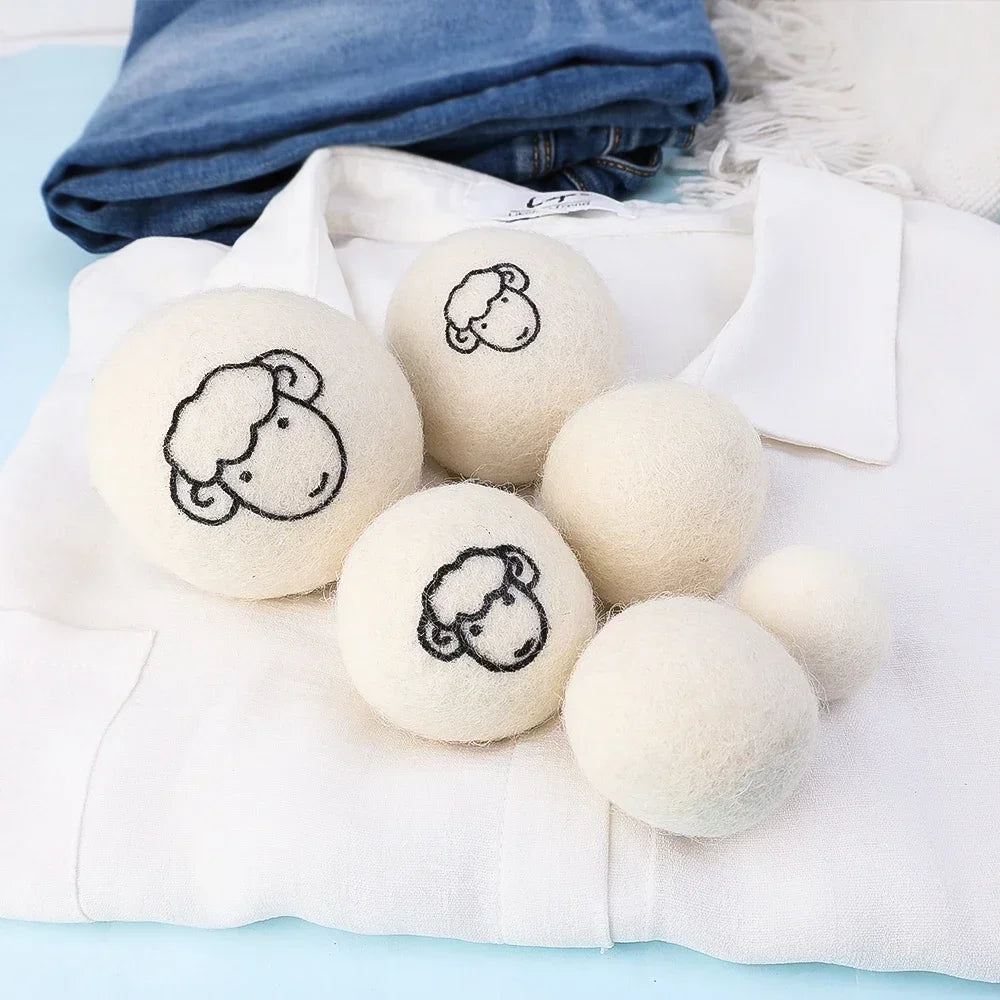 A set of six white wool dryer balls with embroidered sheep faces resting on a white cloth.