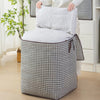 A foldable clothing storage bag with a black and white houndstooth pattern is shown next to a white pillow.
