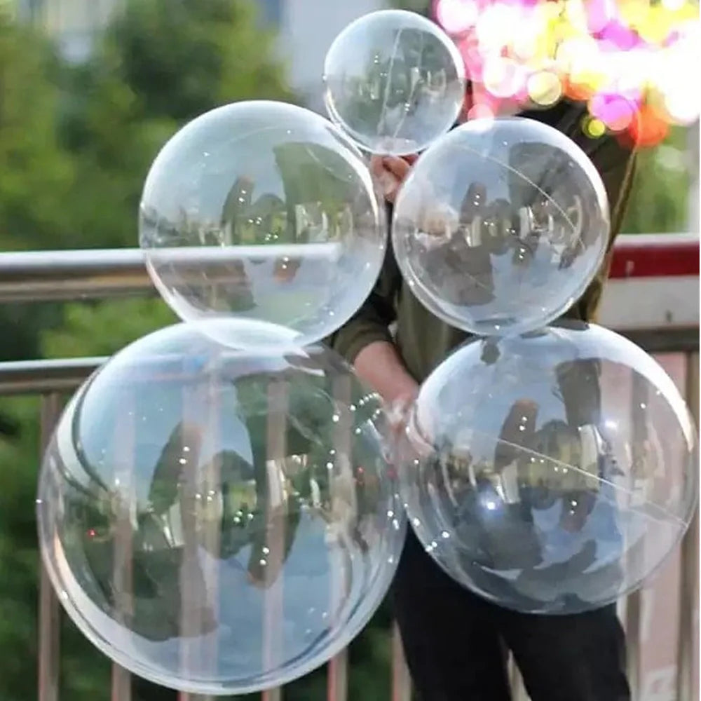 A person is holding several clear latex balloons reflecting the surroundings.
