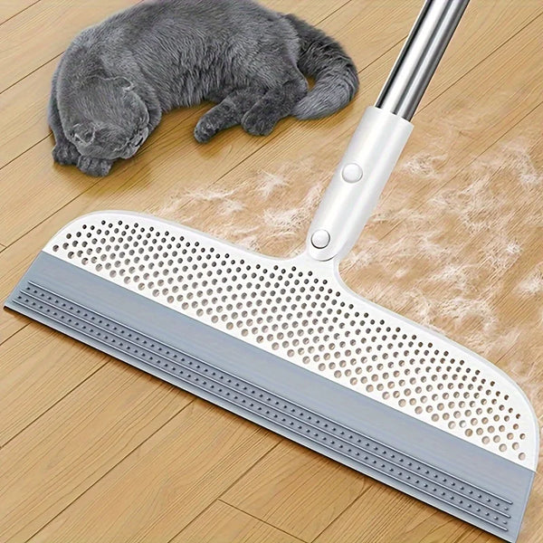 A silver ergonomic broom and scraper set is shown next to a gray kitten on a wooden floor.