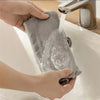 Hands are using a long-handled microfiber duster brush to clean a sink or faucet.