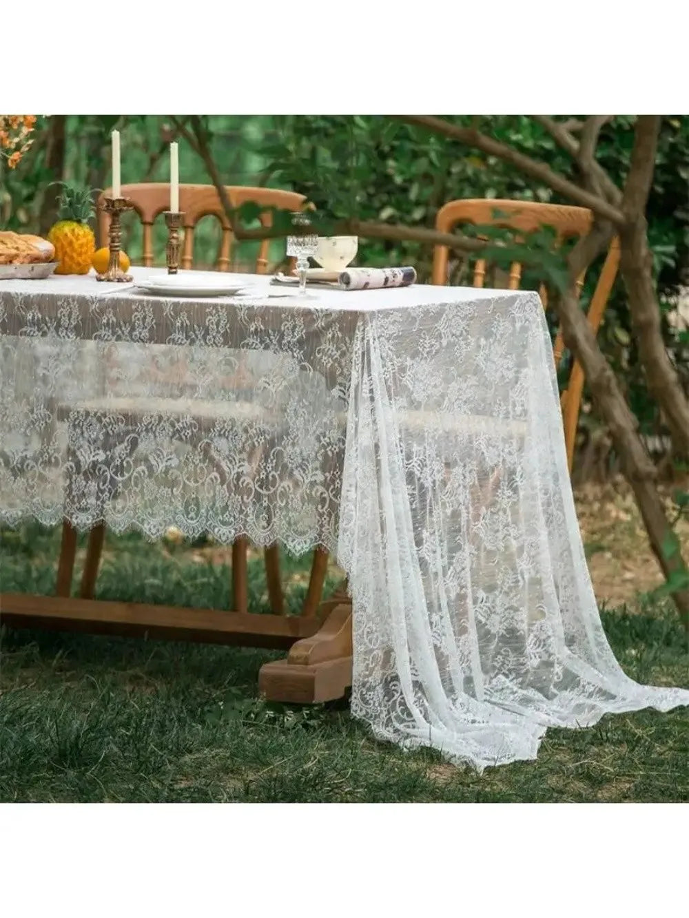 A white lace retro tablecloth is set on an outdoor table surrounded by greenery and wooden chairs.