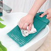 A hand is using a green anti-slip wash basin to clean a white ceramic sink.
