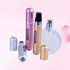 A collection of five portable refillable perfume spray bottles in various metallic shades, including pink, gold, and silver.