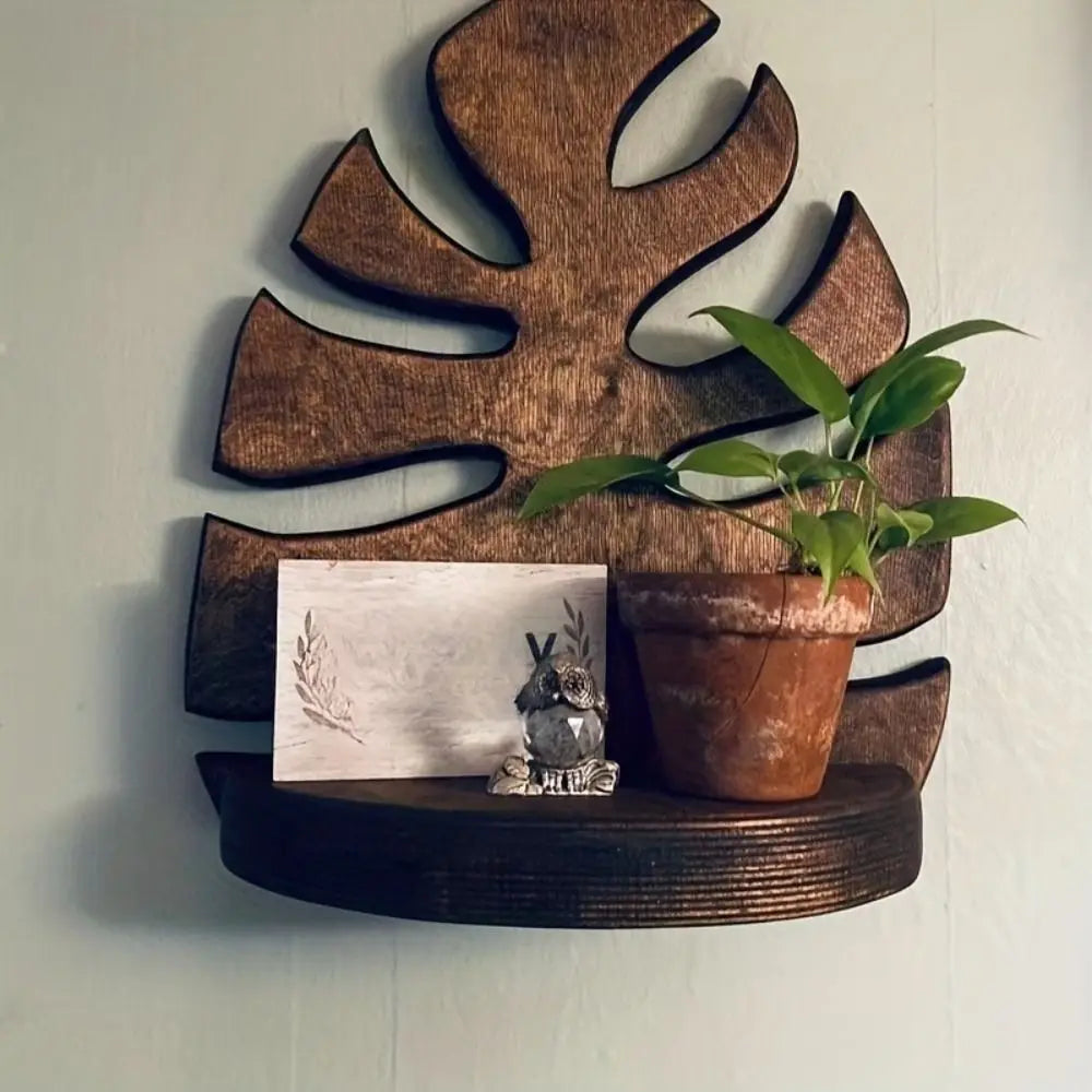 A wooden wall art frame featuring a leaf shape, holding a small potted plant and a decorative stone.