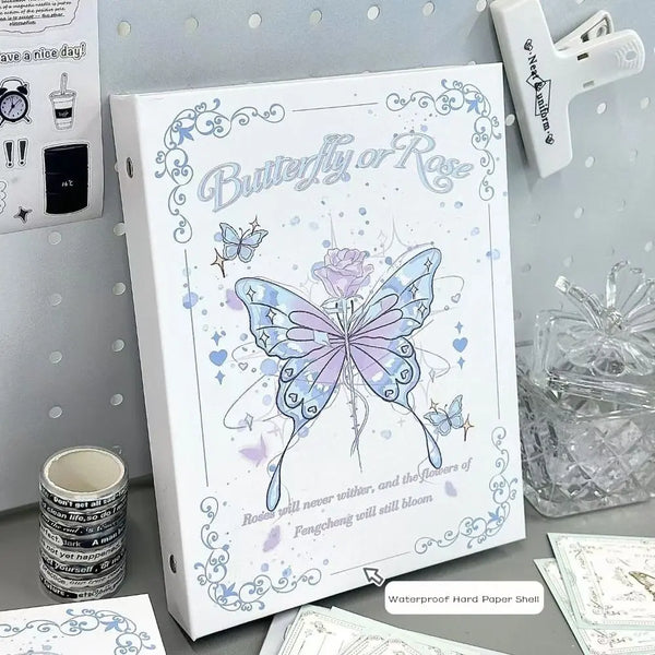 A white photo album featuring a butterfly and rose design on the cover, displayed next to a clear glass and a white plastic i