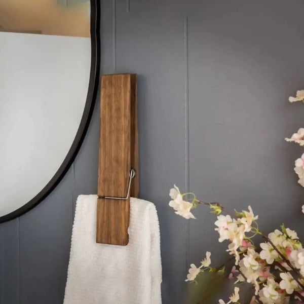 A rustic wooden towel clip hanging on a gray wall next to a mirror and a white towel.