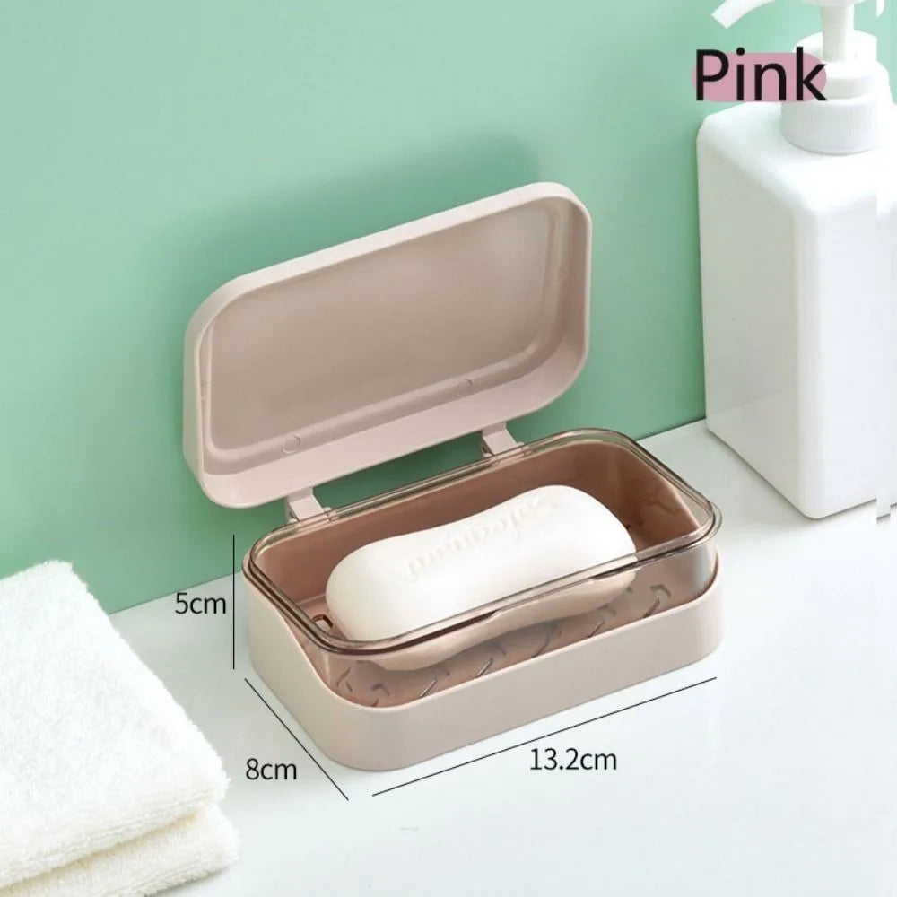 A pink transparent drainage soap dish with a lid and a white bar of soap is shown on a white surface.