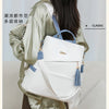 A woman is wearing a sage green jacket and carrying a white leather travel backpack with blue accents.
