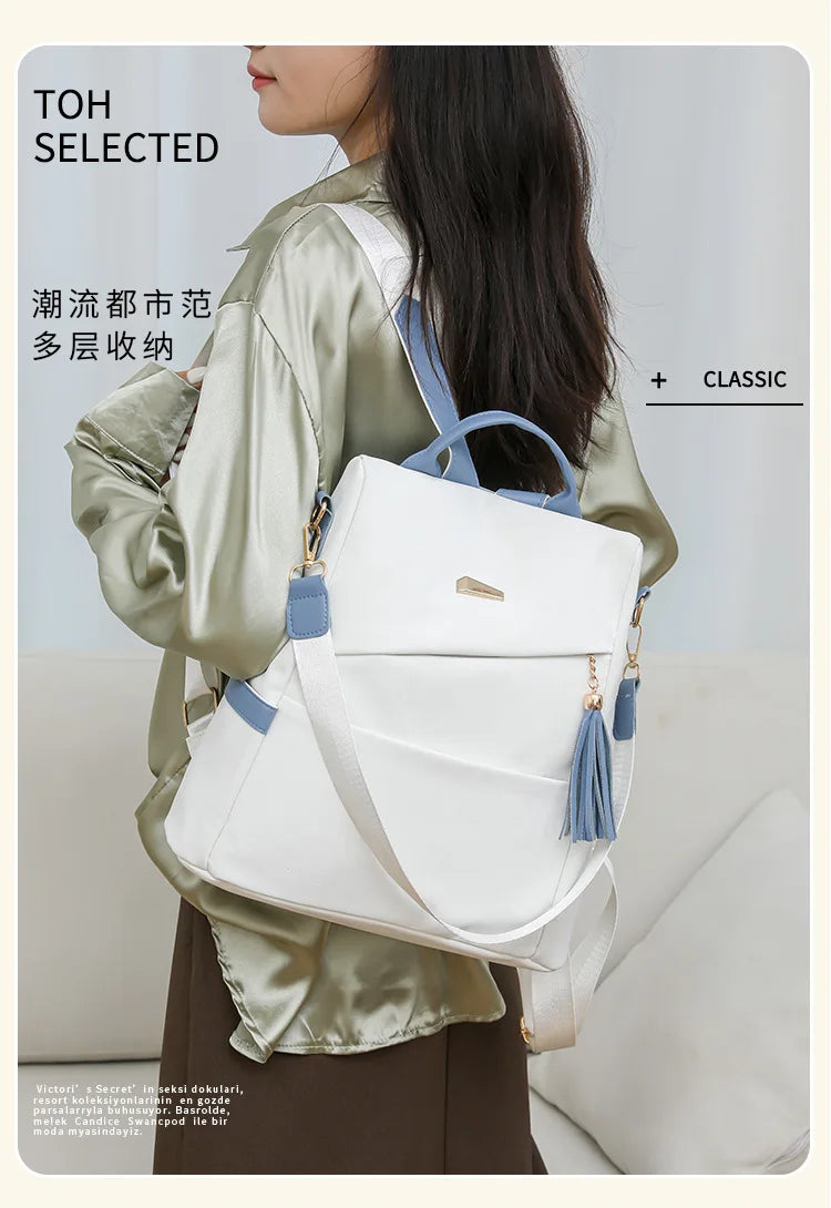 A woman is wearing a sage green jacket and carrying a white leather travel backpack with blue accents.