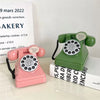 A pink retro telephone money jar with a green cord and a green vintage telephone is displayed on a white surface.