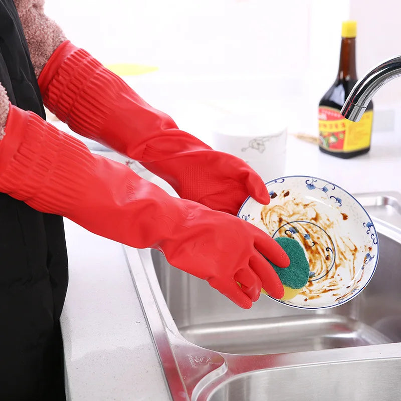 A person wearing red silicone dishwashing gloves is washing dishes in a stainless steel sink.
