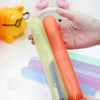 A hand holds two colored silicone toothbrush cases, one light green and one orange.
