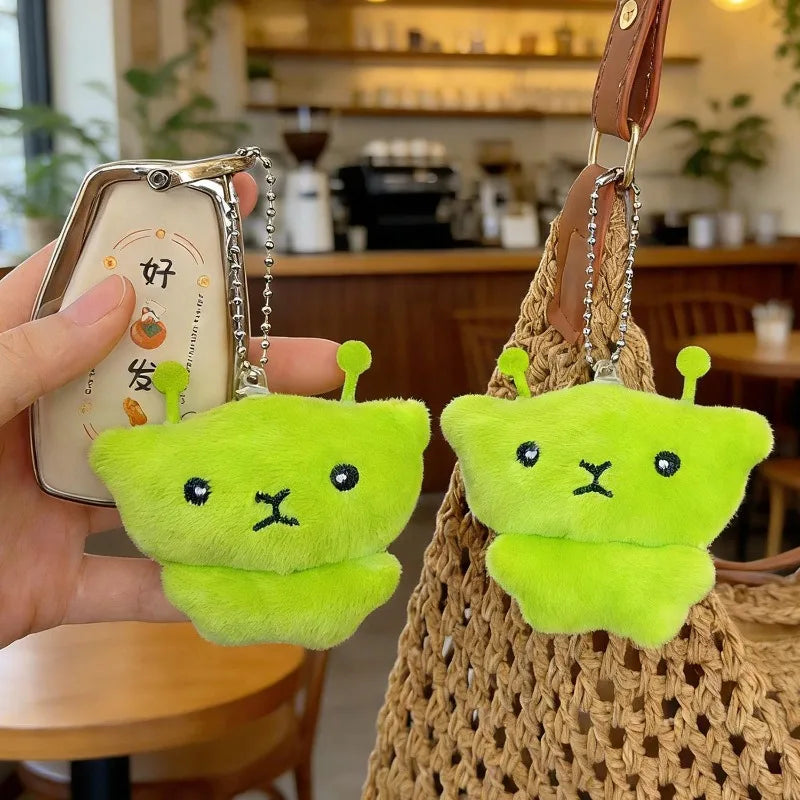 A pair of bright lime green Galaxy Cat plush keychains hanging from a brown woven bag.