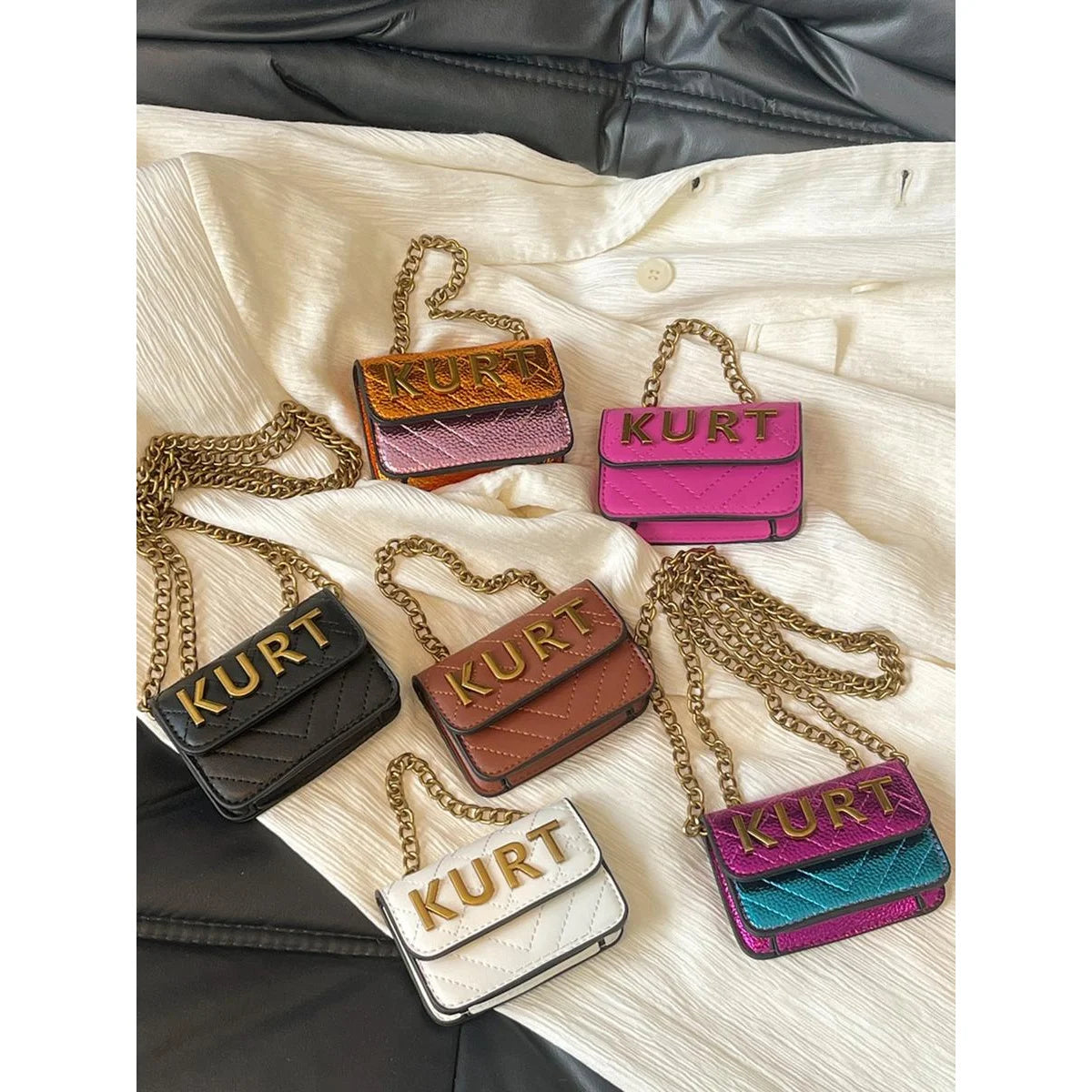 A collection of five magnetic crossbody bags in various colors and finishes displayed on a white shirt.