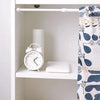 A white shelf displays a white alarm clock, a white cylindrical object, and a white rectangular block next to an adjustable c