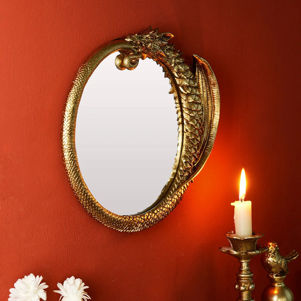 A round, ornate golden mirror hangs on a terracotta wall next to a lit candle and a small golden figurine.