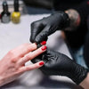 A hand wearing a black nitrile cleaning glove is holding a small object, likely a product, in a close-up shot.