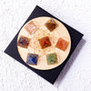 A set of natural stone chakra pyramids arranged on a wooden disc within a black square box.