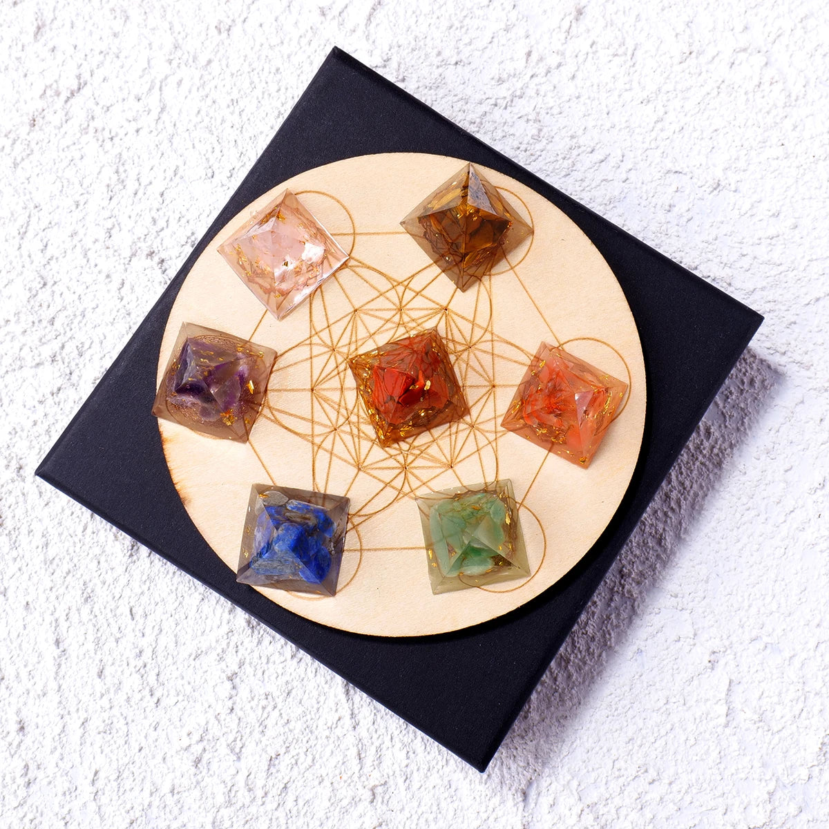 A set of natural stone chakra pyramids arranged on a wooden disc within a black square box.