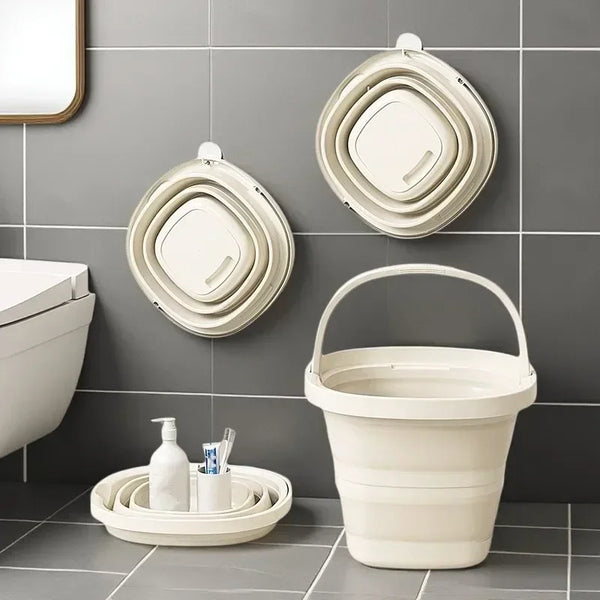 A white collapsible water bucket with a handle is displayed on a gray tiled wall next to various bathroom accessories.