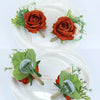 Boutonnière vintage orange soie avec feuillage vert et fleurs blanches sur une assiette blanche.