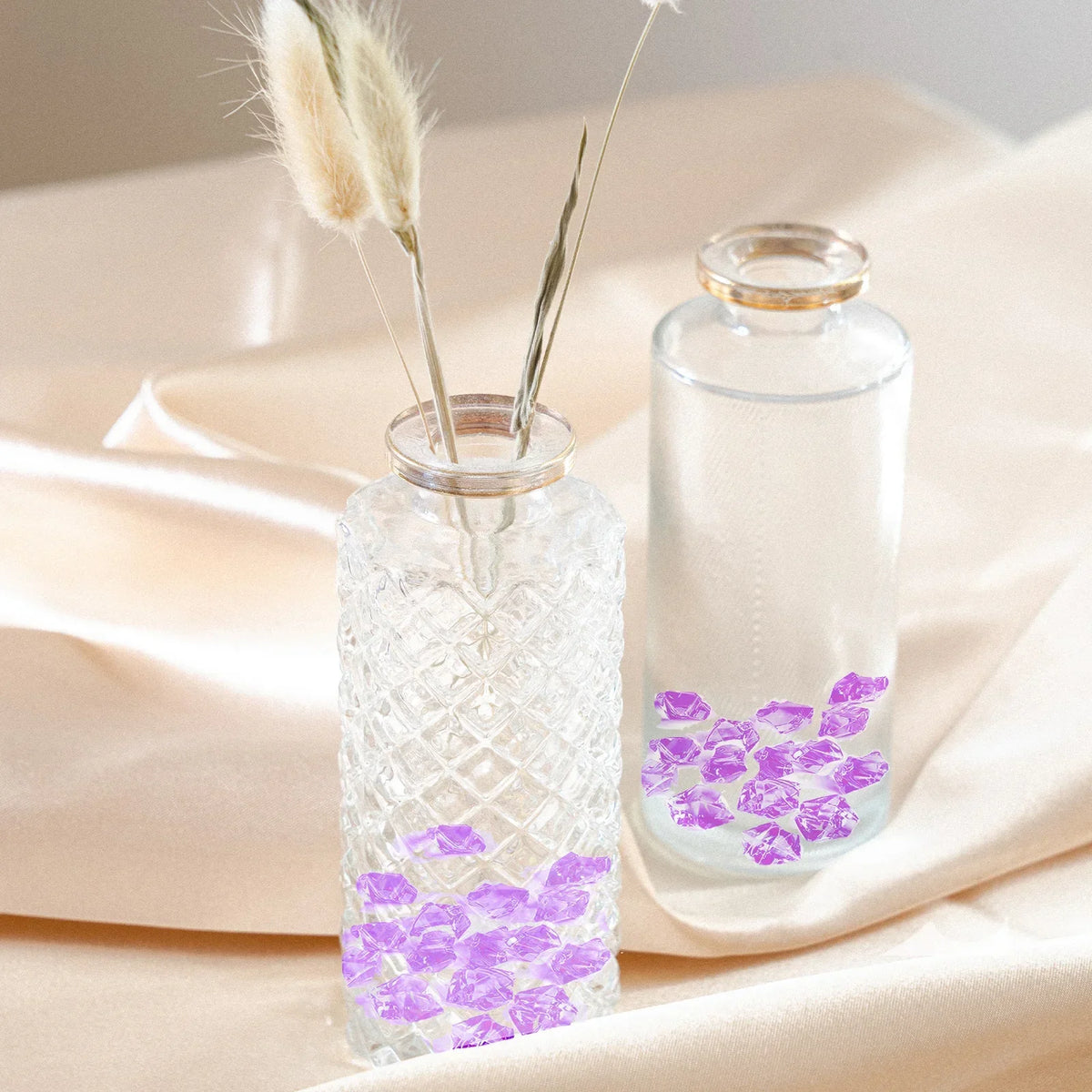 Glass jars filled with purple crushed ice stones and dried floral elements on a beige fabric.