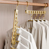A close-up of a wooden clothing rack with gold-toned hangers holding light beige and white garments.