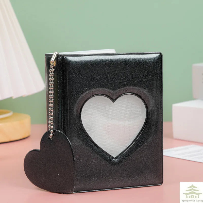 A black mini photo album shaped like a heart with a silver chain detail, resting on a pink surface.