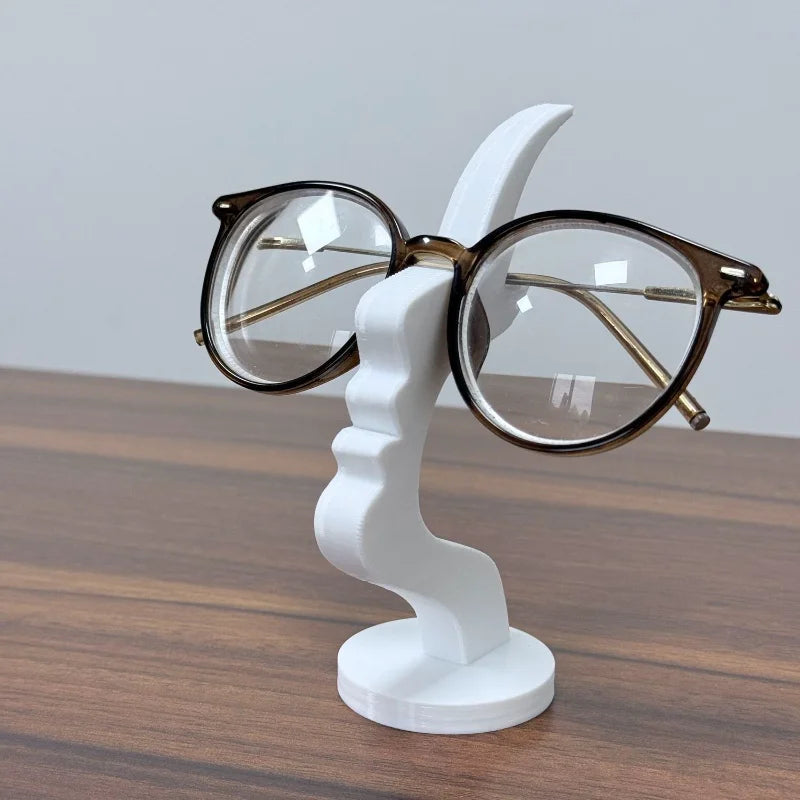 A white 3D printed profile stand for eyeglasses with gold-rimmed lenses resting on a wooden surface.